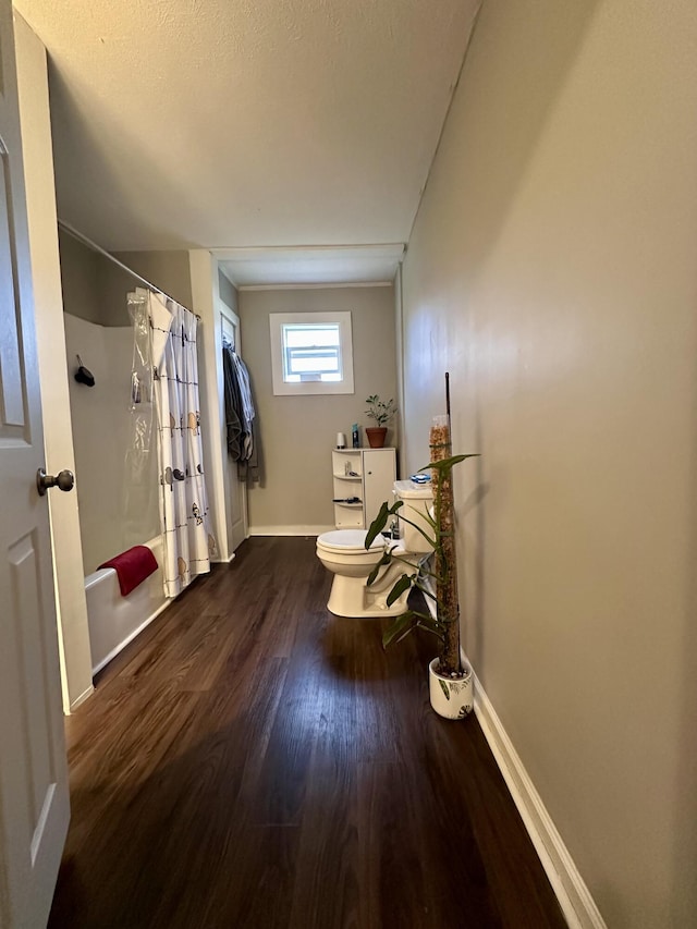 bathroom with shower / bathtub combination with curtain, toilet, wood finished floors, and baseboards