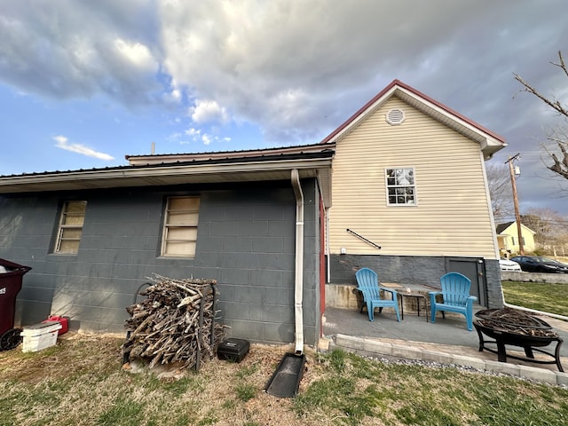 back of house with an outdoor fire pit, concrete block siding, and a patio