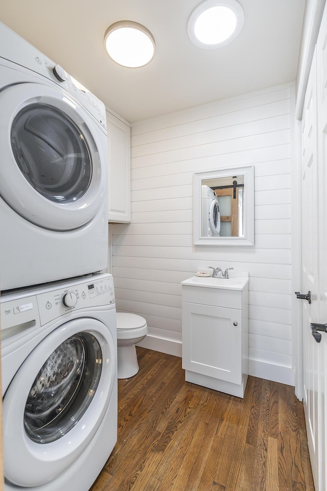 clothes washing area featuring a sink, stacked washer / drying machine, dark wood finished floors, and laundry area