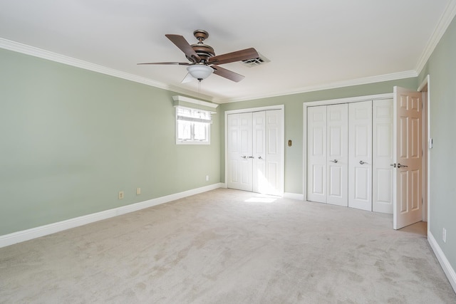 unfurnished bedroom with visible vents, two closets, ornamental molding, carpet floors, and baseboards