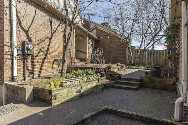 view of side of property featuring a patio area, brick siding, and fence