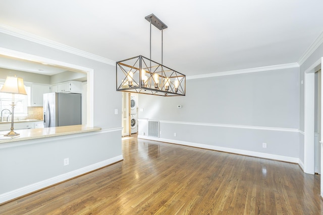 unfurnished dining area with stacked washer / dryer, baseboards, ornamental molding, an inviting chandelier, and wood finished floors