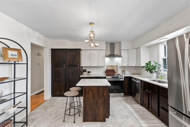 kitchen featuring a center island, wall chimney range hood, a breakfast bar area, appliances with stainless steel finishes, and a sink