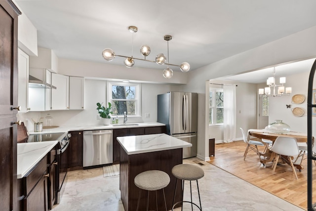 kitchen featuring a sink, dark brown cabinetry, appliances with stainless steel finishes, pendant lighting, and a chandelier