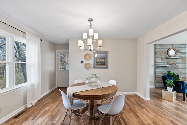 dining space with visible vents, an inviting chandelier, a fireplace, light wood finished floors, and baseboards