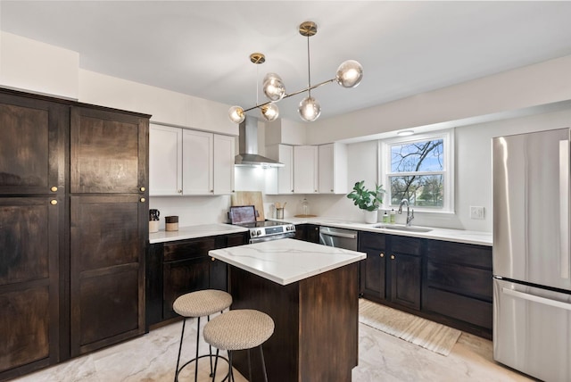 kitchen featuring a breakfast bar, a sink, stainless steel appliances, wall chimney exhaust hood, and a center island