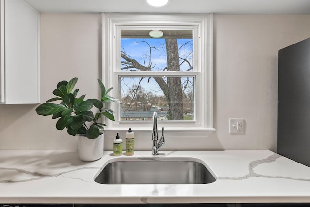 interior details with a sink, light stone counters, and white cabinetry