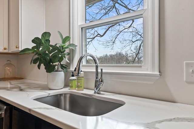 room details with white cabinets, light stone countertops, and a sink