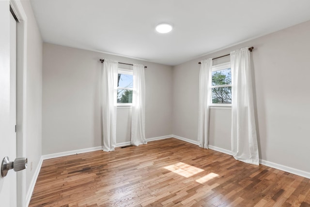 spare room featuring visible vents, light wood-style flooring, baseboards, and a healthy amount of sunlight