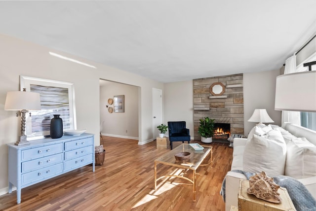 living room with light wood finished floors, a stone fireplace, and baseboards