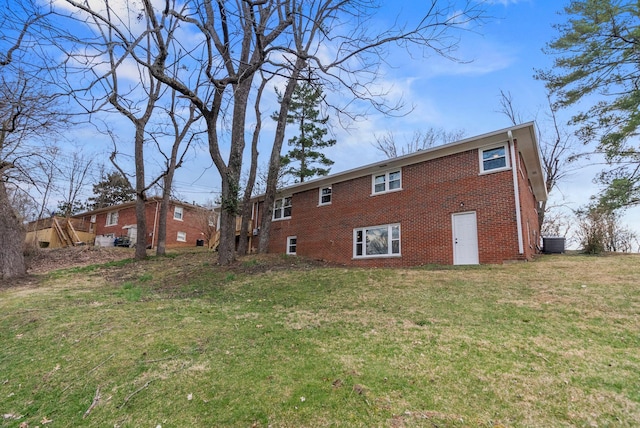 rear view of property featuring brick siding, cooling unit, and a yard