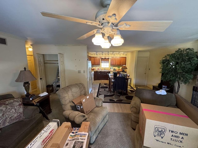 living room with ceiling fan, visible vents, light wood-style flooring, and ornamental molding