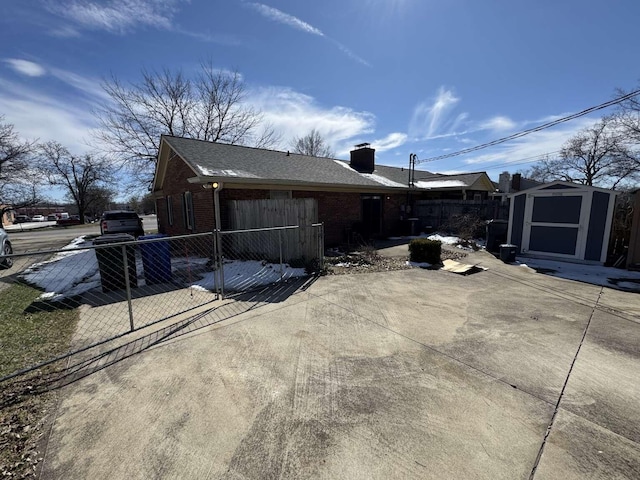 view of side of property featuring brick siding, a shed, fence private yard, an outdoor structure, and a patio