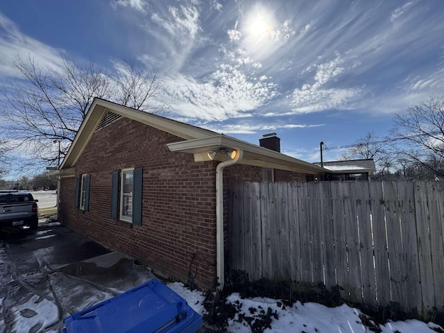 view of side of home with brick siding, a chimney, and fence