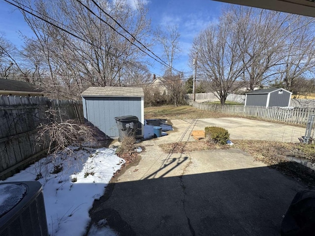 view of yard featuring concrete driveway, a storage shed, a fenced backyard, a patio area, and an outbuilding