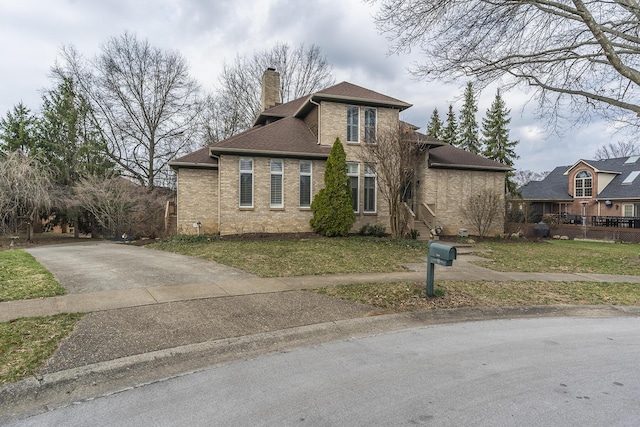 view of front facade featuring brick siding, a front lawn, concrete driveway, roof with shingles, and a chimney