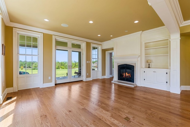 unfurnished living room with light wood-type flooring, built in shelves, ornamental molding, a fireplace, and baseboards