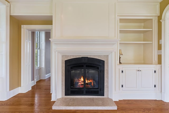 details featuring a glass covered fireplace, baseboards, built in shelves, and wood finished floors