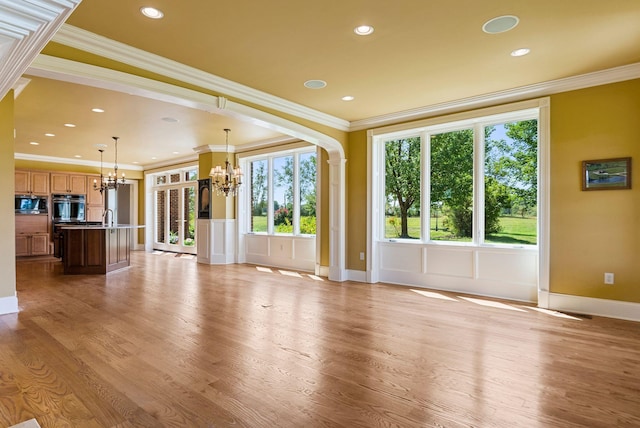 unfurnished living room with ornamental molding, light wood-type flooring, and a chandelier