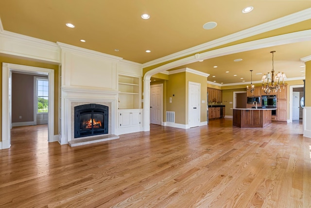 unfurnished living room featuring visible vents, a chandelier, light wood-type flooring, a glass covered fireplace, and a sink