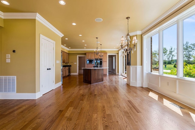 kitchen featuring visible vents, a kitchen island with sink, ornamental molding, wood finished floors, and a chandelier