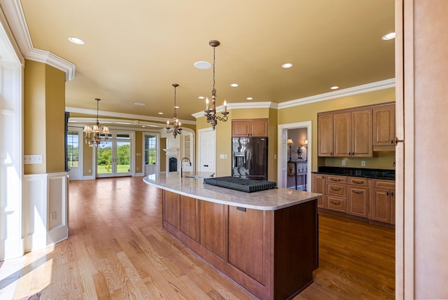 kitchen with an inviting chandelier, a large island with sink, a sink, black fridge with ice dispenser, and light wood-type flooring