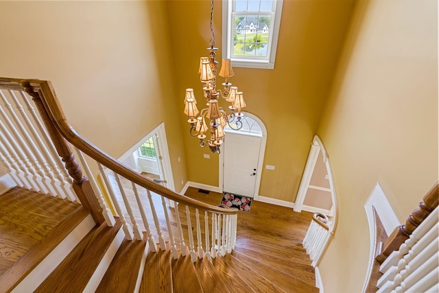 foyer entrance with baseboards, stairs, a high ceiling, wood finished floors, and a notable chandelier