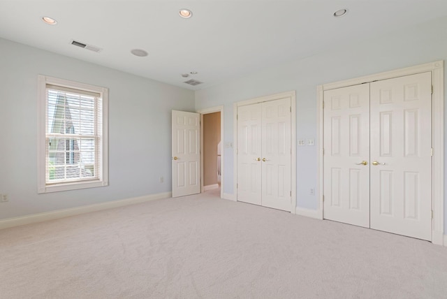 unfurnished bedroom with visible vents, two closets, baseboards, light colored carpet, and recessed lighting