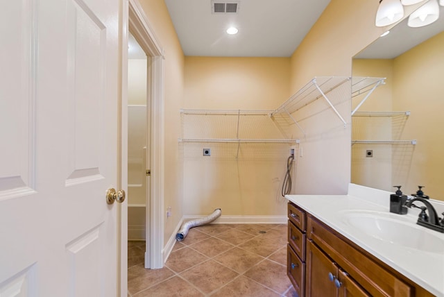 bathroom with tile patterned flooring, visible vents, a walk in closet, baseboards, and vanity