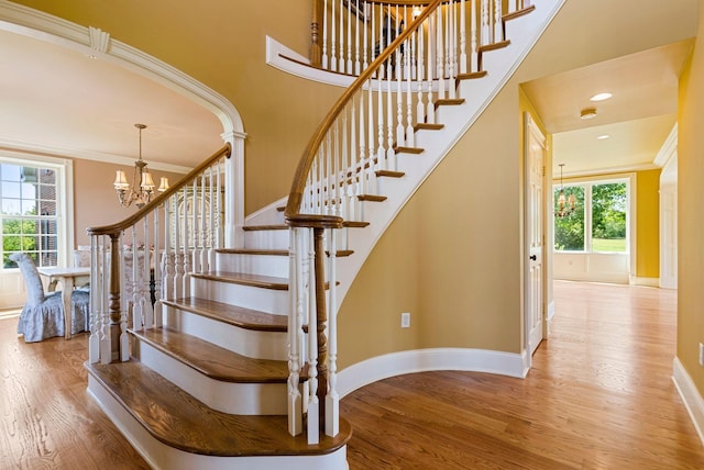 stairway featuring a notable chandelier, wood finished floors, baseboards, and ornamental molding