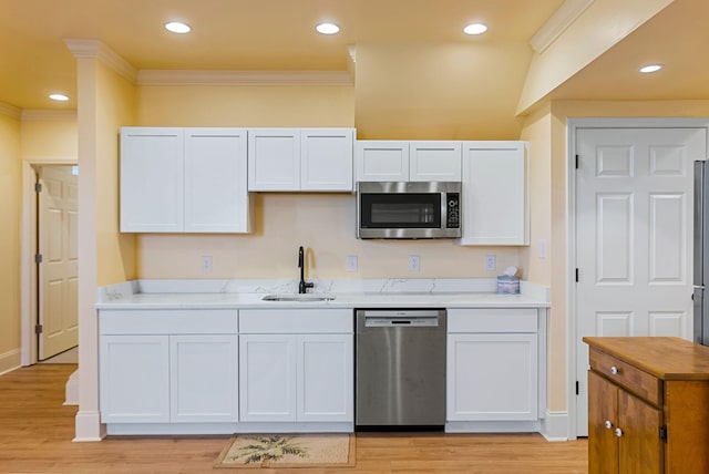 kitchen featuring a sink, appliances with stainless steel finishes, white cabinets, crown molding, and light wood finished floors