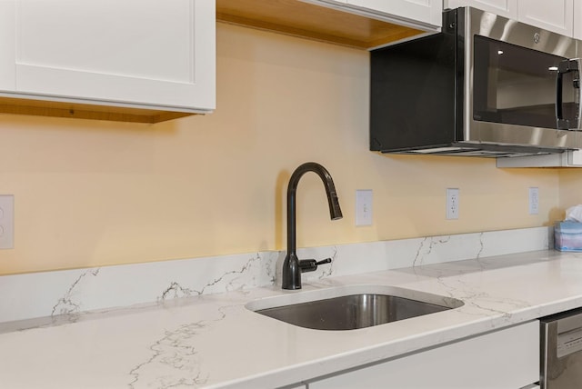 kitchen with a sink, stainless steel appliances, light stone counters, and white cabinets