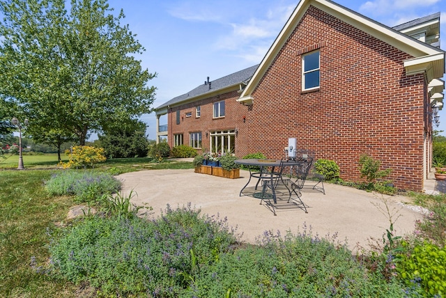 back of property featuring brick siding, a lawn, and a patio