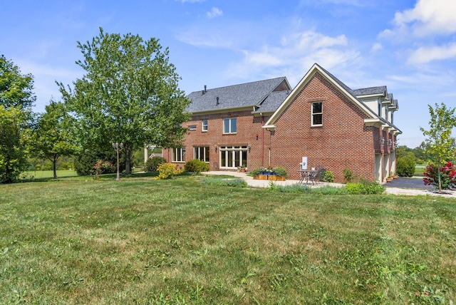 rear view of property featuring a lawn, an attached garage, brick siding, and a patio area