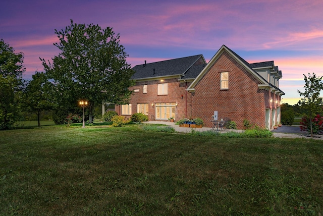 back of property at dusk featuring a yard and brick siding