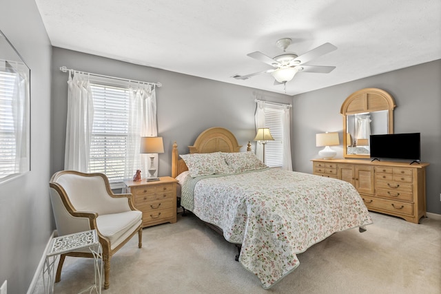 bedroom featuring baseboards, multiple windows, light colored carpet, and ceiling fan