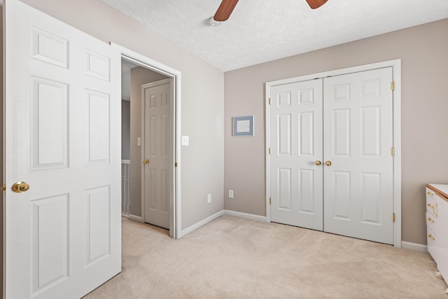 unfurnished bedroom featuring baseboards, light carpet, a textured ceiling, and a closet