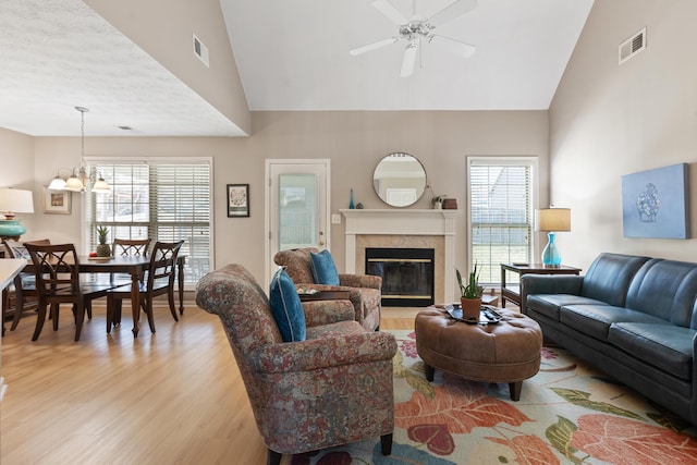 living room featuring visible vents, light wood finished floors, high vaulted ceiling, a fireplace, and ceiling fan with notable chandelier