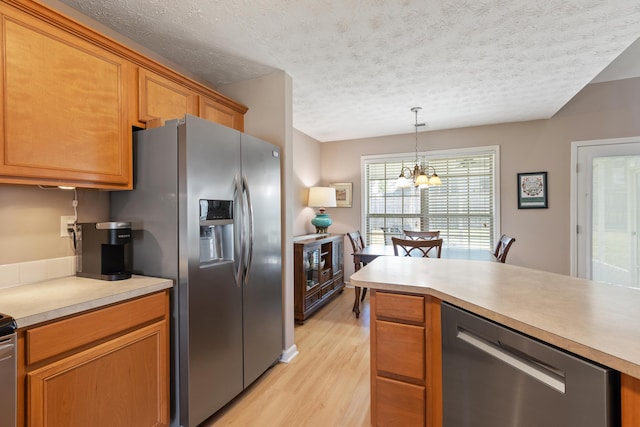 kitchen with light wood finished floors, decorative light fixtures, appliances with stainless steel finishes, light countertops, and a chandelier