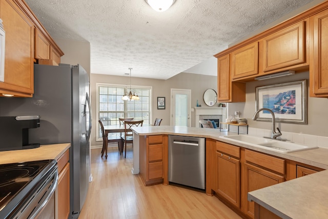 kitchen with light wood-type flooring, light countertops, a peninsula, stainless steel appliances, and a sink