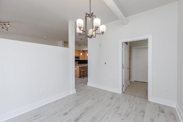 unfurnished room featuring light wood-style flooring, baseboards, and an inviting chandelier