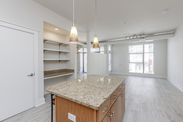 kitchen with brown cabinets, a center island, a breakfast bar area, light wood finished floors, and light stone countertops