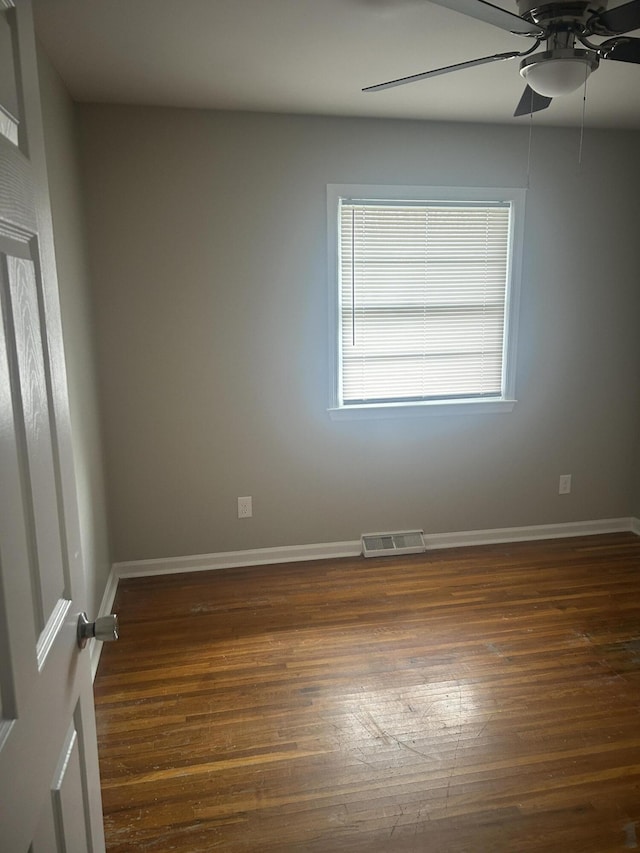 empty room with wood finished floors, a ceiling fan, visible vents, and baseboards