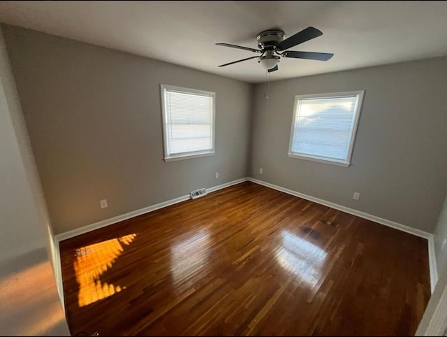 empty room featuring a wealth of natural light, visible vents, dark wood-type flooring, and ceiling fan