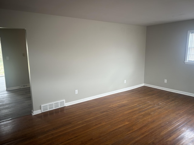 spare room featuring visible vents, baseboards, and dark wood finished floors