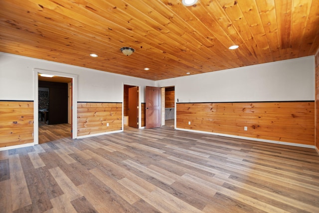 empty room featuring wooden walls, wainscoting, wood ceiling, and wood finished floors