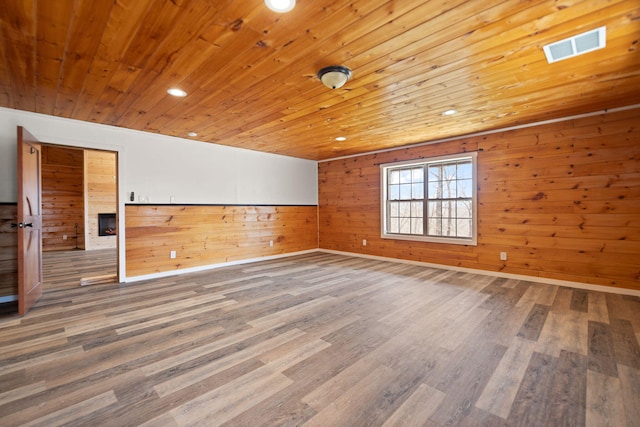 unfurnished room with wooden ceiling, wood finished floors, visible vents, and wood walls