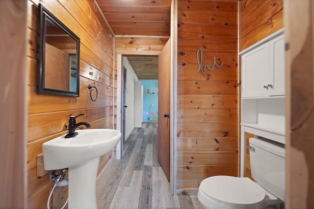 half bathroom featuring toilet, a sink, wood finished floors, wood walls, and wooden ceiling