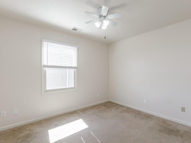 spare room featuring ceiling fan, baseboards, visible vents, and light carpet