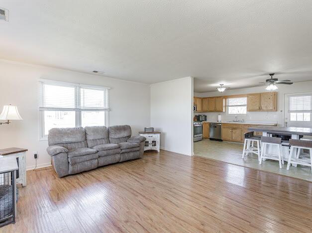 living room featuring visible vents, ceiling fan, a fireplace, and light wood finished floors